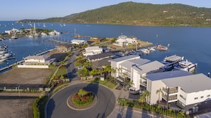 A marina with boats docked, a roundabout, and buildings with modern architecture. - Harbour Cove (Airlie Beach)