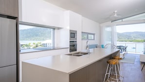 A modern kitchen with a large island, built-in appliances, and a view of the mountains. - Harbour Cove (Airlie Beach)