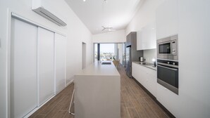 A modern kitchen with white cabinetry, a central island, and stainless steel appliances. - Harbour Cove (Airlie Beach)