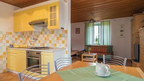 A compact kitchen with yellow cabinets, a gas stove, and a tiled backsplash. There is a dining area with a table set for two, a sofa, and a window with curtains. - Amazing home in Kostel with WiFi (Kostel)