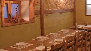 A dining area with a long wooden table set for a meal, a stone wall, and a window with a view of plants. - Amazing home in Kostel with WiFi (Kostel)
