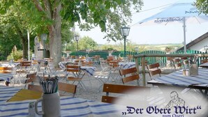 An outdoor dining area with tables and chairs, a large umbrella, and a view of the countryside. - Der Obere Wirt zum Queri (Andechs)