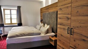 A bedroom with a bed, a nightstand, a wardrobe, and a window with curtains. - Der Obere Wirt zum Queri (Andechs)