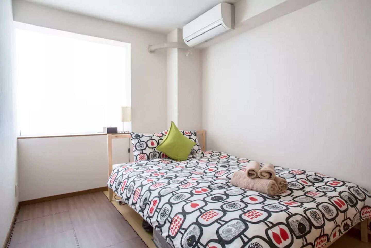 A small, neatly arranged bedroom with a bed, a pillow, and a window.