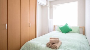 A bedroom with a bed, a green pillow, and rolled towels. - Not Ninja Osaka Namba 1 (Osaka)