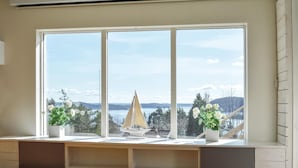 Ein Zimmer mit großem Fenster und Blick auf eine reizvolle Landschaft, einem Schreibtisch mit einem Modellschiff und zwei Zimmerpflanzen.