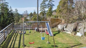 Ein umzäunter Spielplatz im Freien mit Schaukeln, einer Rutsche und einem kleinen Pool.