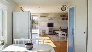 Eine moderne Küche mit weißen Schränken, ein Essbereich mit weißem Tisch und Stühlen sowie ein Wohnbereich mit Sofa und Fernseher.