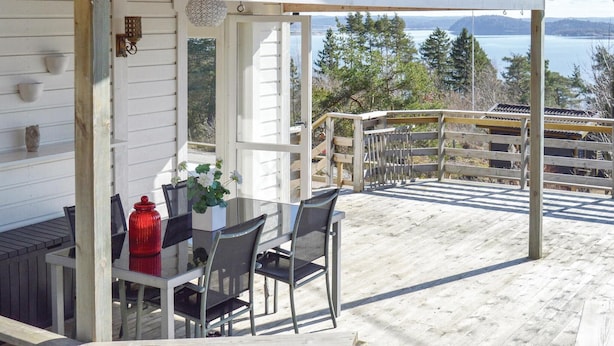 Eine überdachte Terrasse mit Tisch und Stühlen mit Blick auf einen See und bewaldete Hügel.