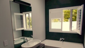 A modern bathroom with a freestanding bathtub, a large mirror, and a window with blinds.