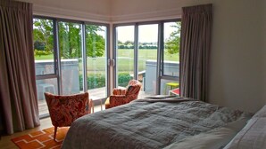 A bedroom with a large bed, a chair, and a view of a garden through a sliding glass door.