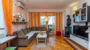Ein modernes Wohnzimmer mit einer Couch, einem Couchtisch und einem Fernseher. Es gibt eine Küchenzeile mit einem Herd und Schränken.
