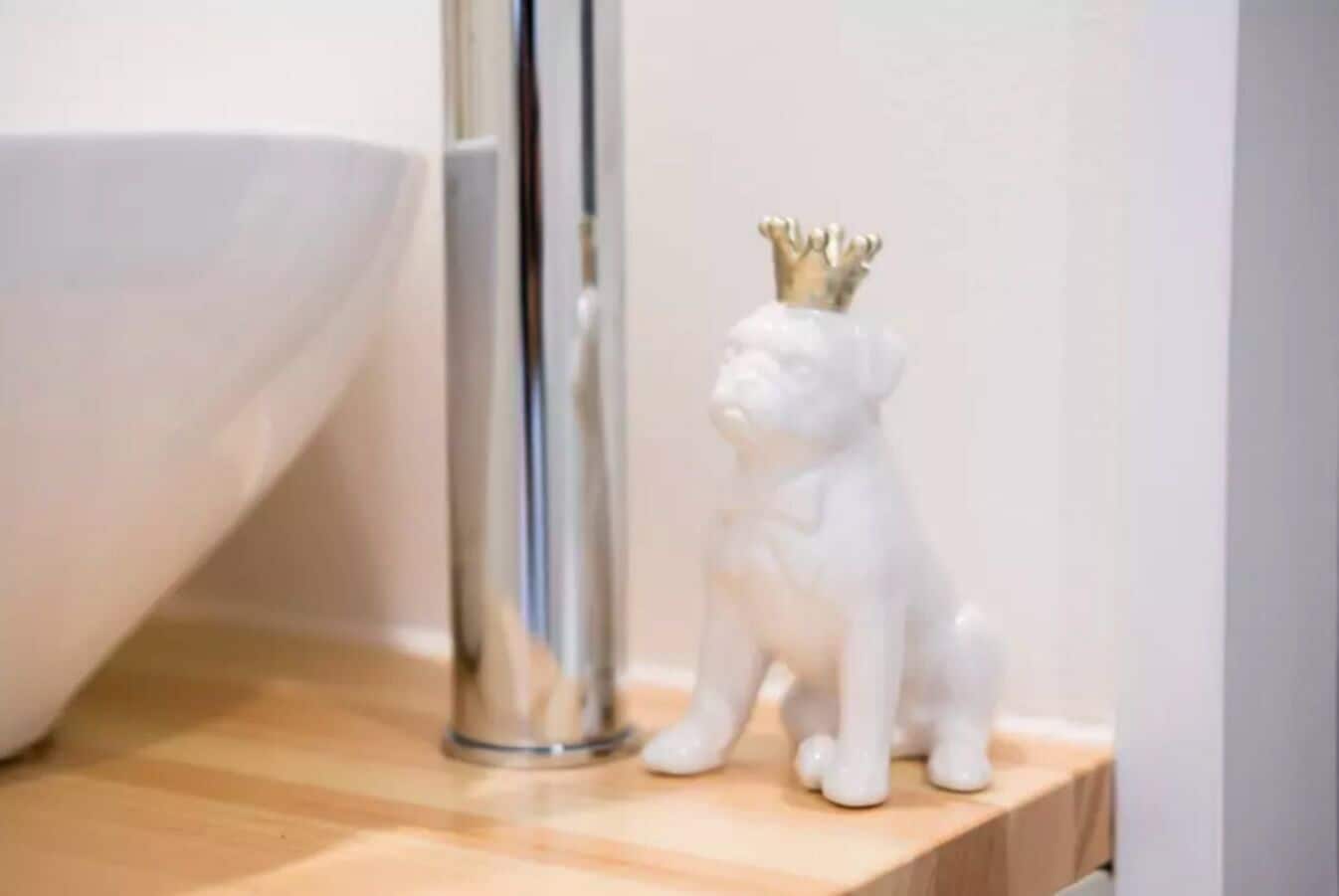 A white ceramic figurine with a gold crown sitting next to a white bowl on a wooden surface.