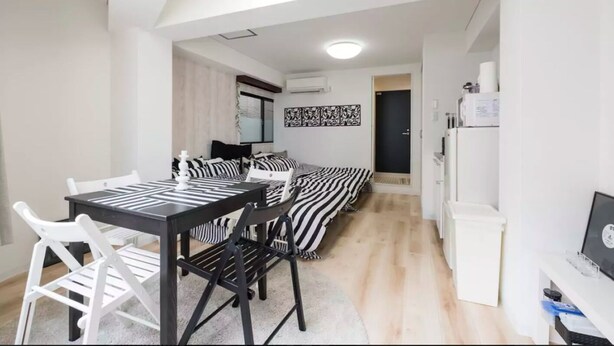 Een moderne, compacte leefruimte met een eethoek, een bed met gestreepte beddengoed en een kitchenette.
