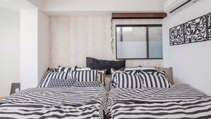 Een slaapkamer met twee bedden, gestreept beddengoed, een raam met zonwering, een airconditioner en een wanddecoratie.