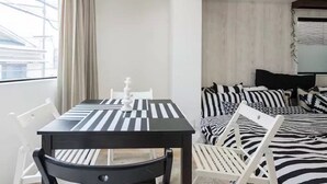 Een kamer met een tafel en stoelen met strepen, een bed met zebraprint beddengoed, en een raam met gordijnen.