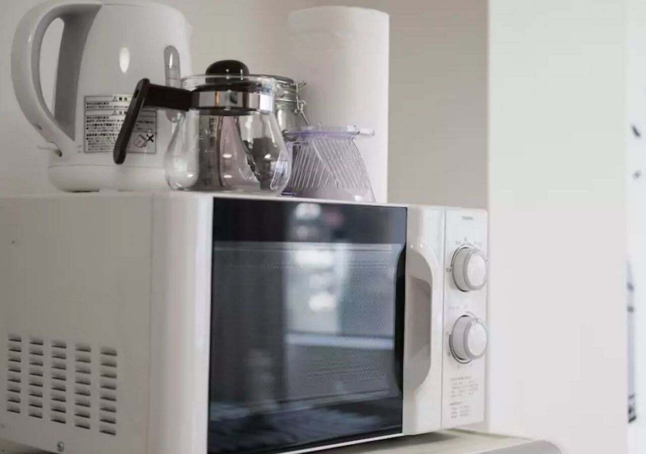 A microwave with a coffee maker and a glass container on top.