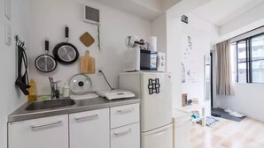 Een kleine keuken met een spoelbak, fornuis en magnetron. Er hangen keukengerei en een kleine plant aan de muur.