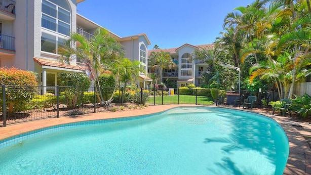A swimming pool surrounded by lush greenery and a multi-story building with balconies. - Beautiful 2 Bedroom Retreat  ( 1 min from tramline) (Surfers Paradise)