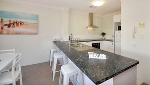 A modern kitchen with a marble countertop, white bar stools, a painting on the wall, and a built-in stove. - Beautiful 2 Bedroom Retreat  ( 1 min from tramline) (Surfers Paradise)