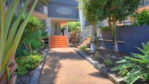 A pathway leading to a building with a sign reading "Villas Siena". - Beautiful 2 Bedroom Retreat  ( 1 min from tramline) (Surfers Paradise)