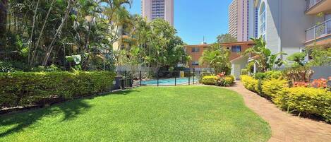 A well-maintained courtyard with a swimming pool, surrounded by lush greenery and tall buildings in the background.