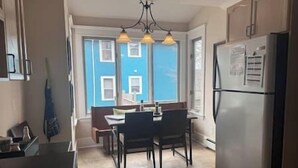 Een keuken met een eettafel, stoelen, een koelkast en een raam met blauwe luiken.