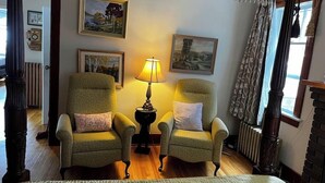 Een kamer met twee fauteuils, een tafel met een lamp en ingelijste foto's aan de muur.