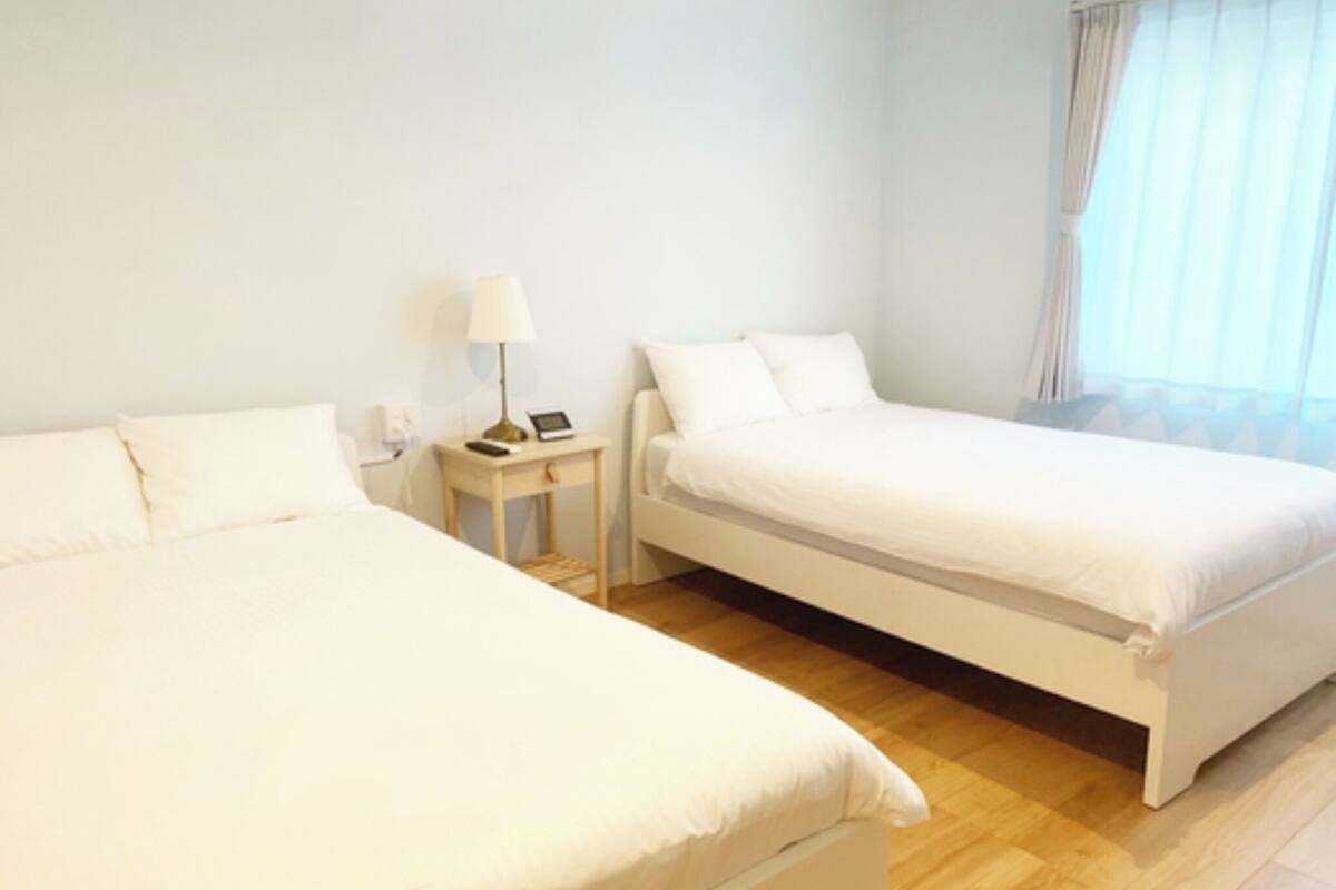 Une chambre d’hôtel avec deux lits simples, une table de chevet avec une lampe et une fenêtre avec des rideaux.