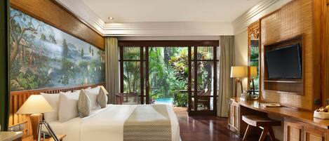 A spacious hotel room with a large bed, a desk, a television, and a view of a lush garden.