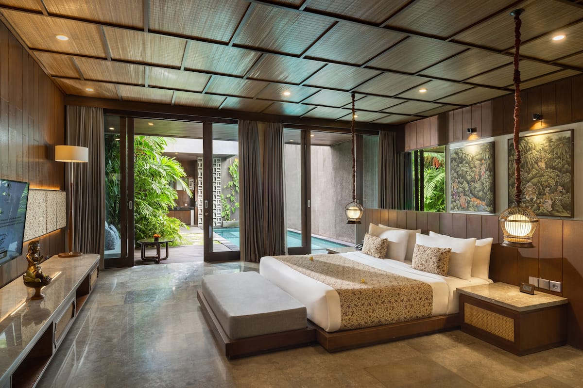 A spacious bedroom with a large bed, a TV, and a view of a pool and greenery.