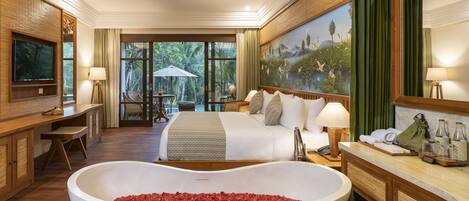 A spacious hotel room with a large bed, a sitting area with a view, a large bathtub filled with rose petals, and a painting on the wall.