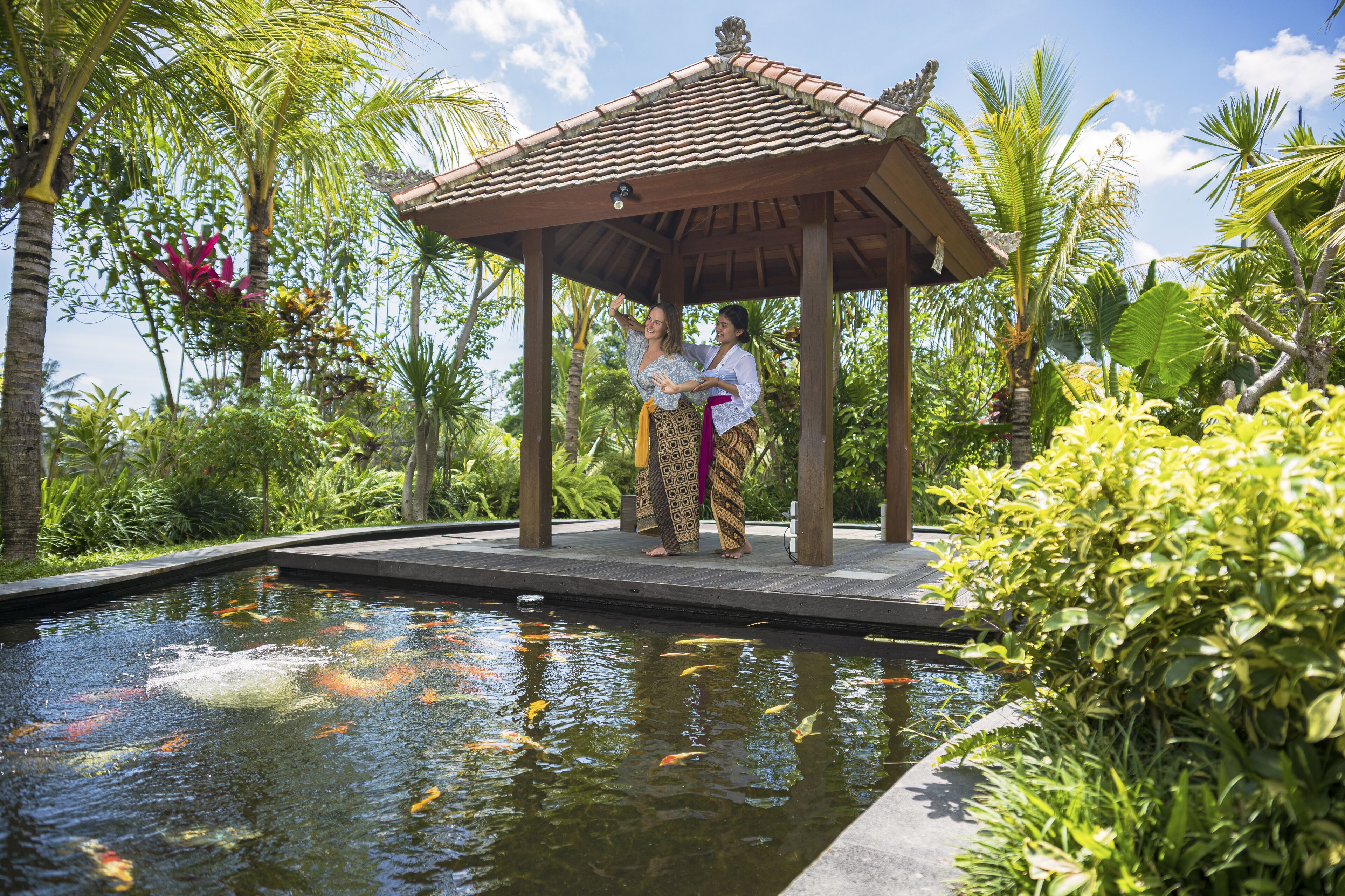 A covered pavilion with a tiled roof, surrounded by lush greenery and a koi pond.