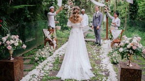 Una ceremonia de boda en un jardín exuberante con una novia en vestido blanco, rodeada de invitados y decoración floral.