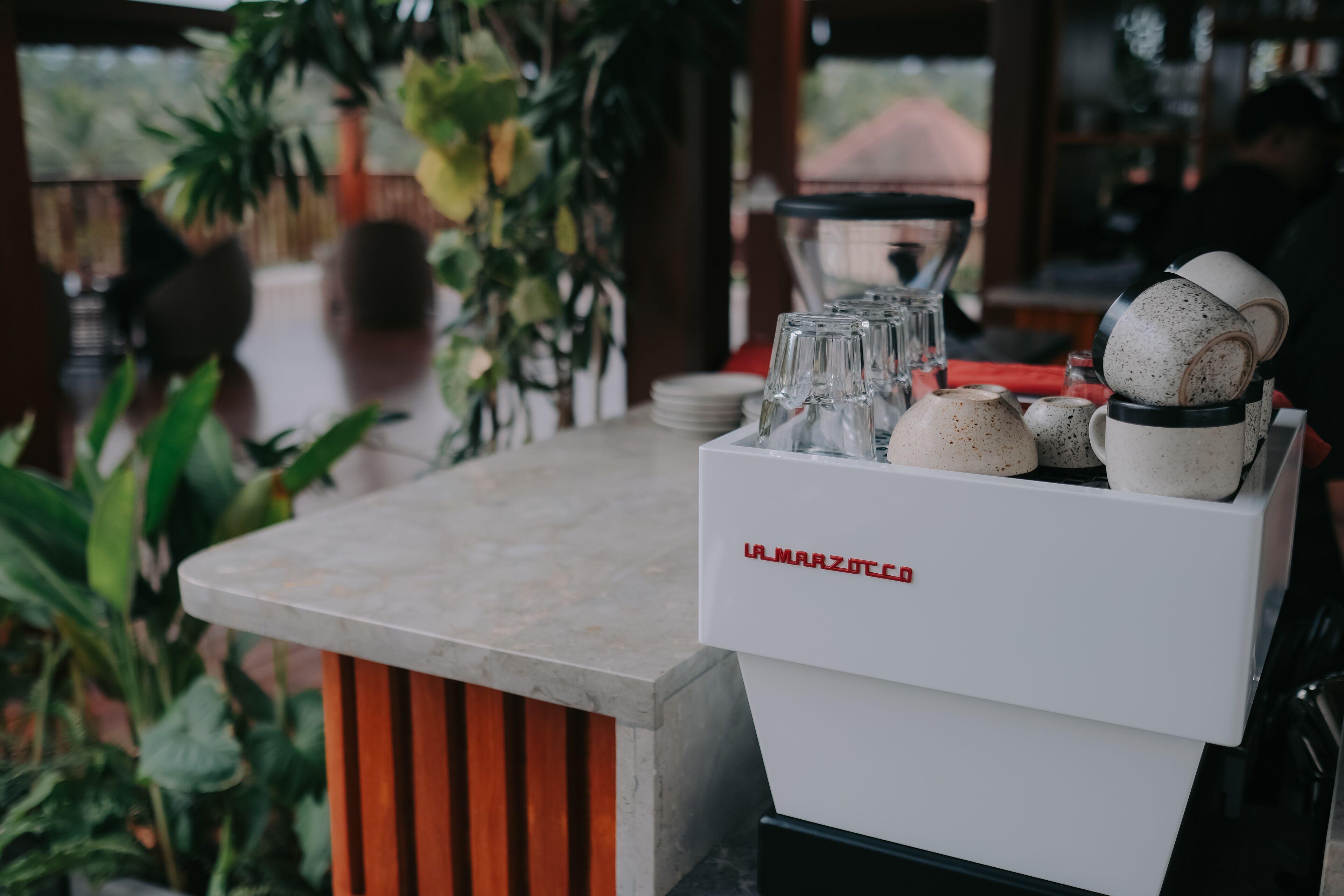 A bar area with a marble countertop, a coffee machine, and a variety of glassware and ceramic mugs.
