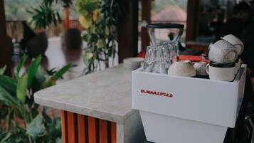 A bar area with a marble countertop, a coffee machine, and a variety of glassware and ceramic mugs.