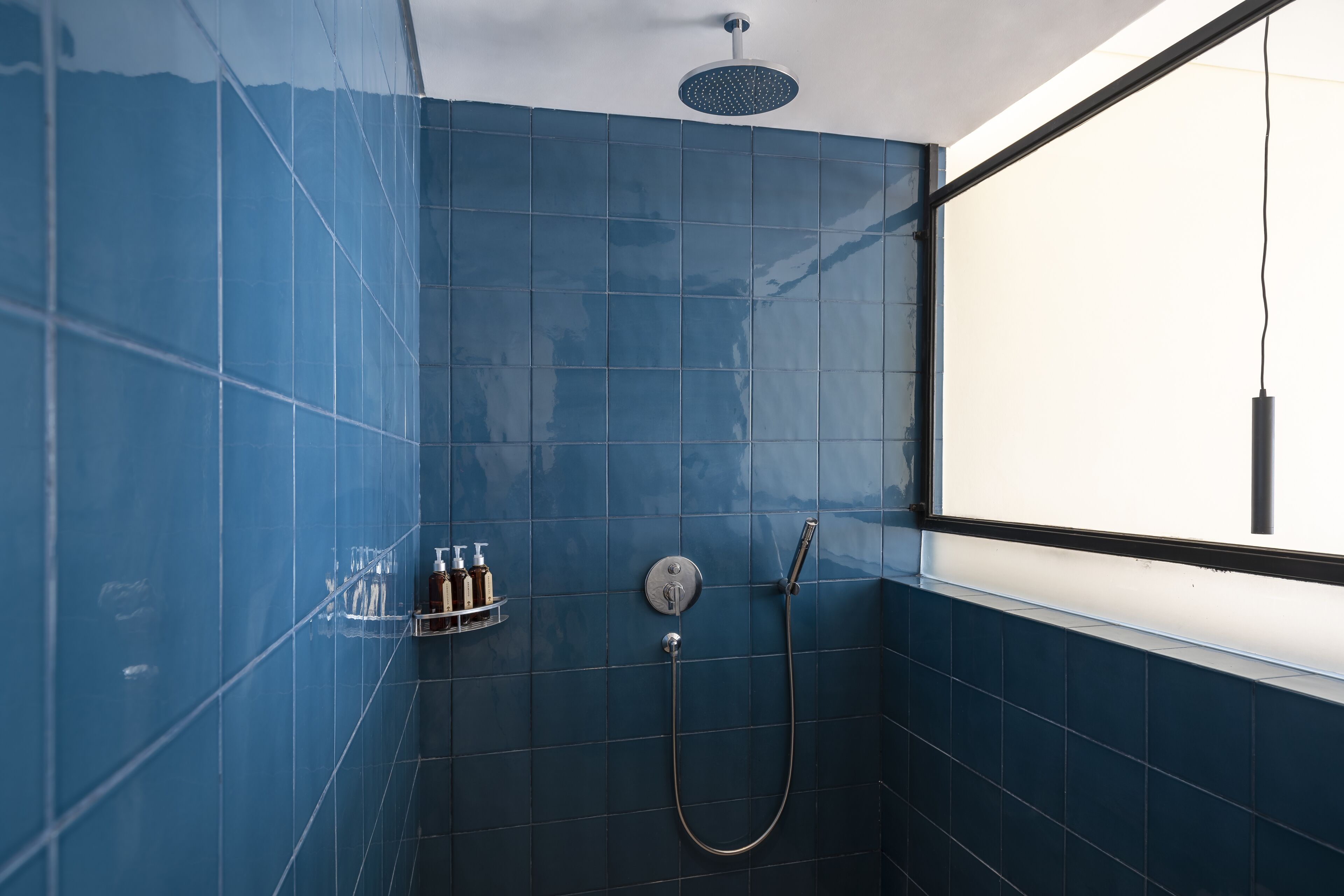 Un baño con azulejos azules, ducha y ventana.