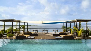 A rooftop infinity pool with lounge chairs and tables, overlooking a body of water. - Adiwana Warnakali Resort (Penida Island)