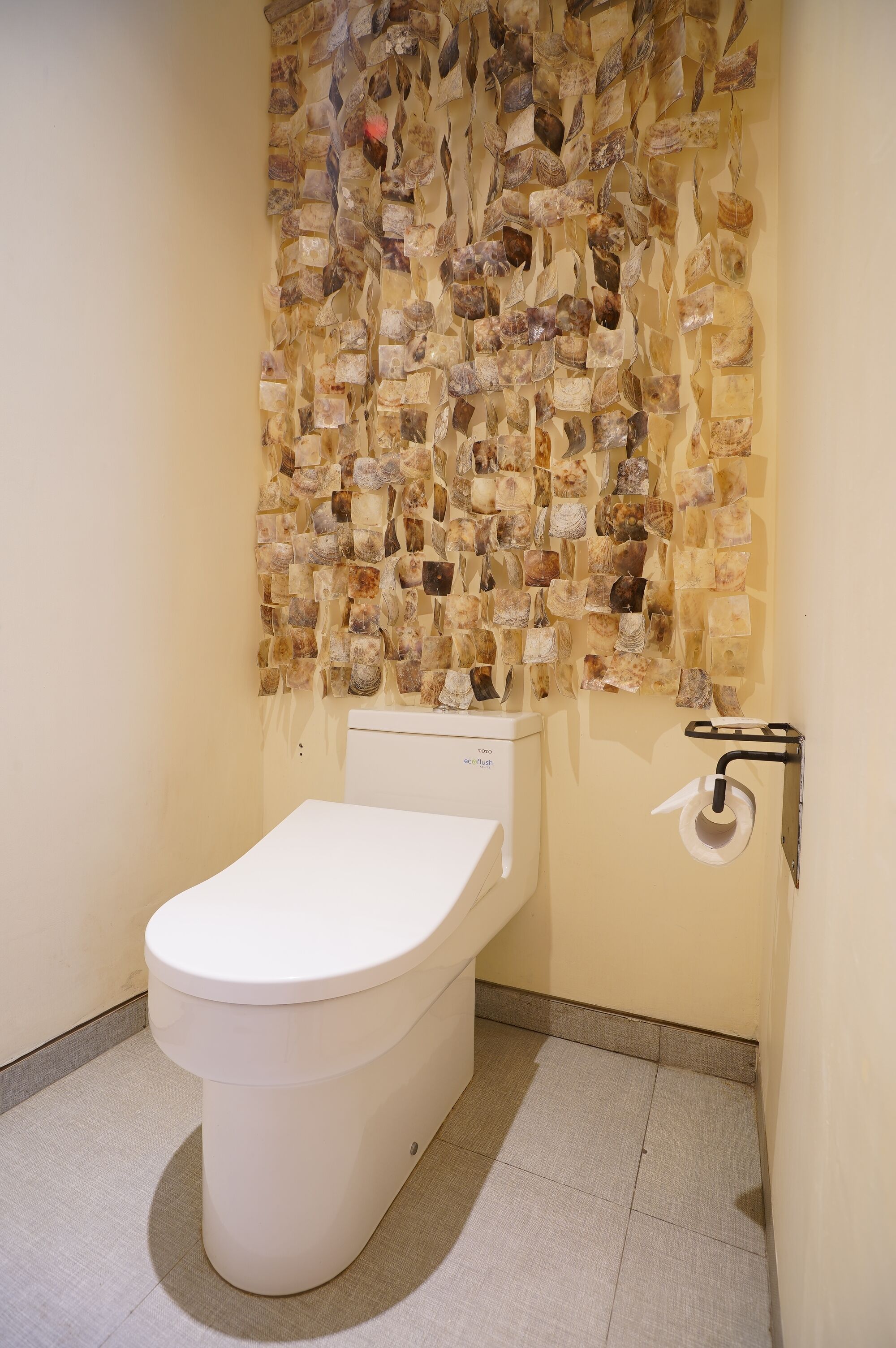 Casa de banho com sanita, suporte de papel higiénico na parede e chão em mosaico.