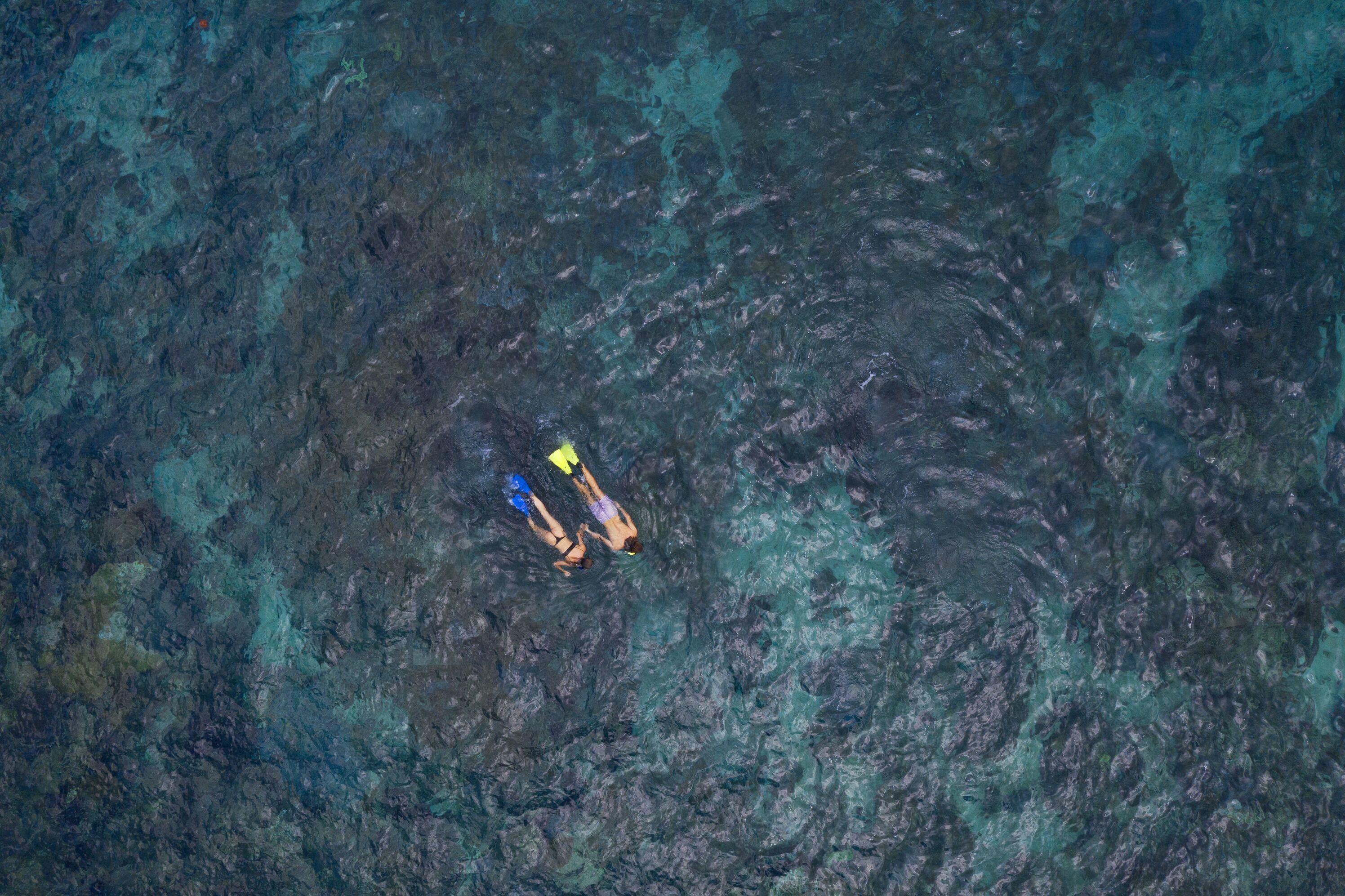 Vista aérea de una playa con agua turquesa cristalina y terreno rocoso.