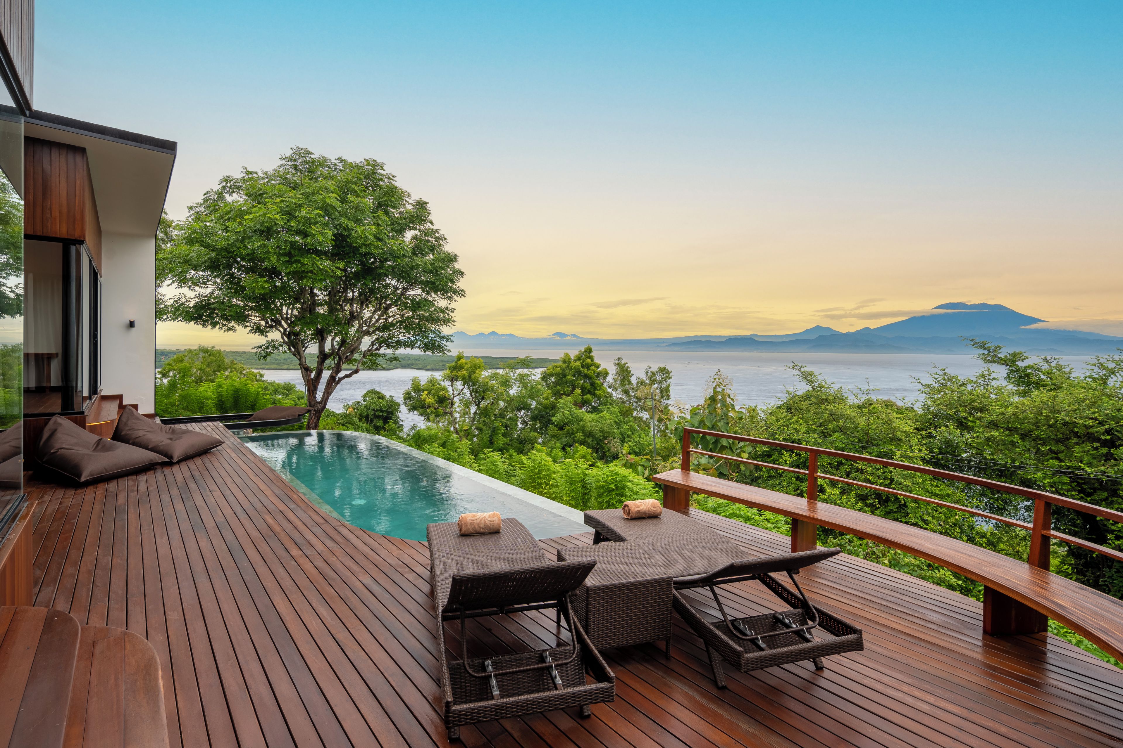 Une terrasse en bois avec une piscine, des chaises longues et une vue sur les montagnes.