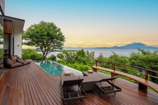 Une terrasse en bois avec une piscine, des chaises longues et une vue sur les montagnes.