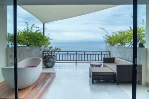 Un balcón con vista al mar, una bañera grande y mobiliario exterior.