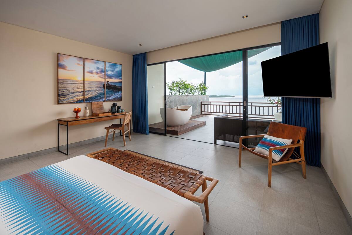 A hotel room with a bed, a desk, a chair, a TV, and a balcony with a view.