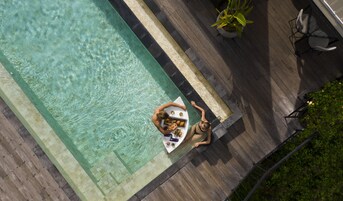 Vista aérea de una piscina con terraza de madera y zona de estar con sillas y una mesa.