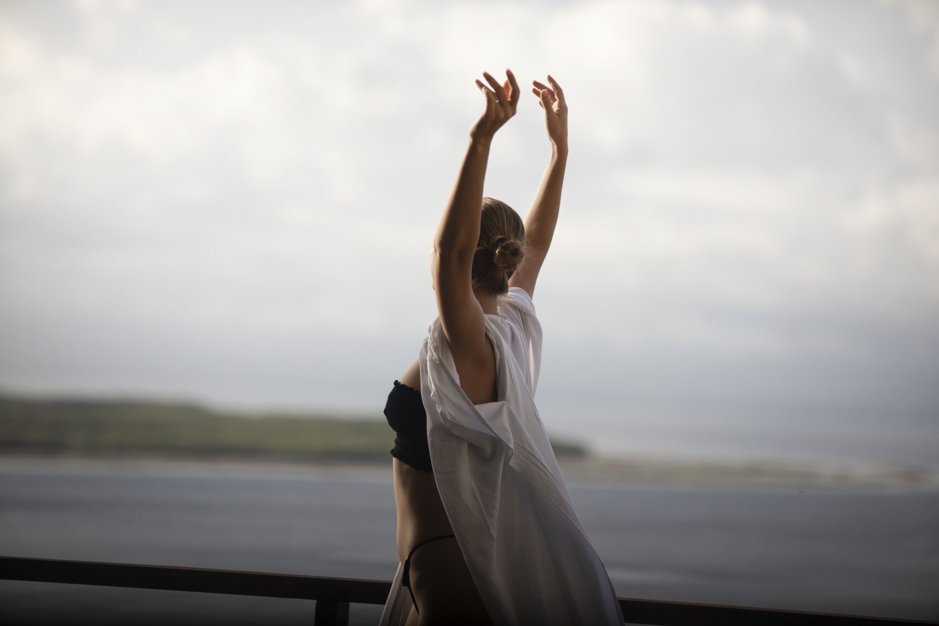A person standing with arms raised, overlooking a body of water.