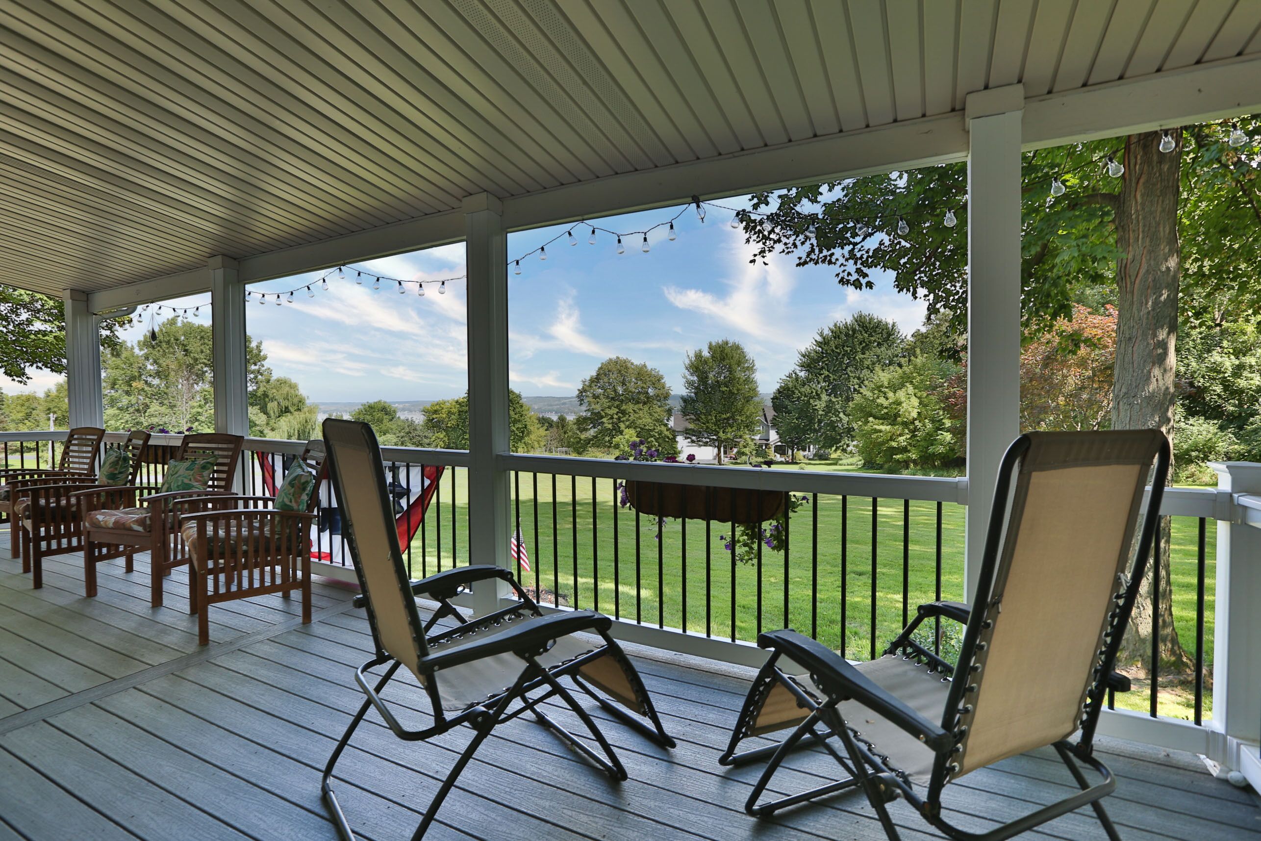 Eine überdachte Veranda mit Holzstühlen und einem Tisch, mit Blick auf eine grüne Landschaft mit Bäumen und blauem Himmel.