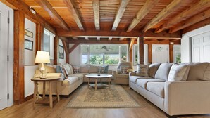 A cozy living room with wooden beams, a beige sofa, a round coffee table, and a rug. - Whole House, Scenic Post and Beam Home Overlooking Canandaigua Lake! Sleeps 10 (Canandaigua)
