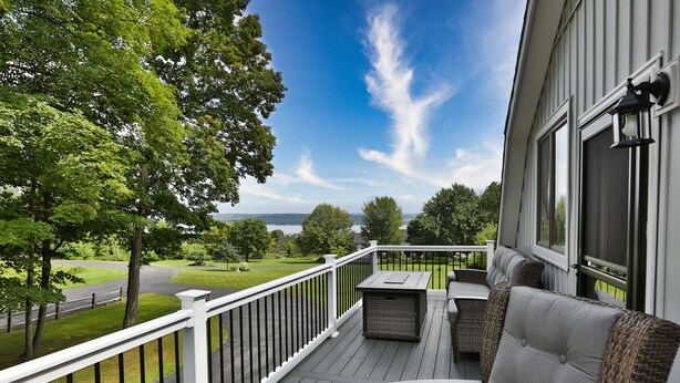 A deck with outdoor furniture, a white railing, and a view of a green landscape. - Whole House, Scenic Post and Beam Home Overlooking Canandaigua Lake! Sleeps 10 (Canandaigua)