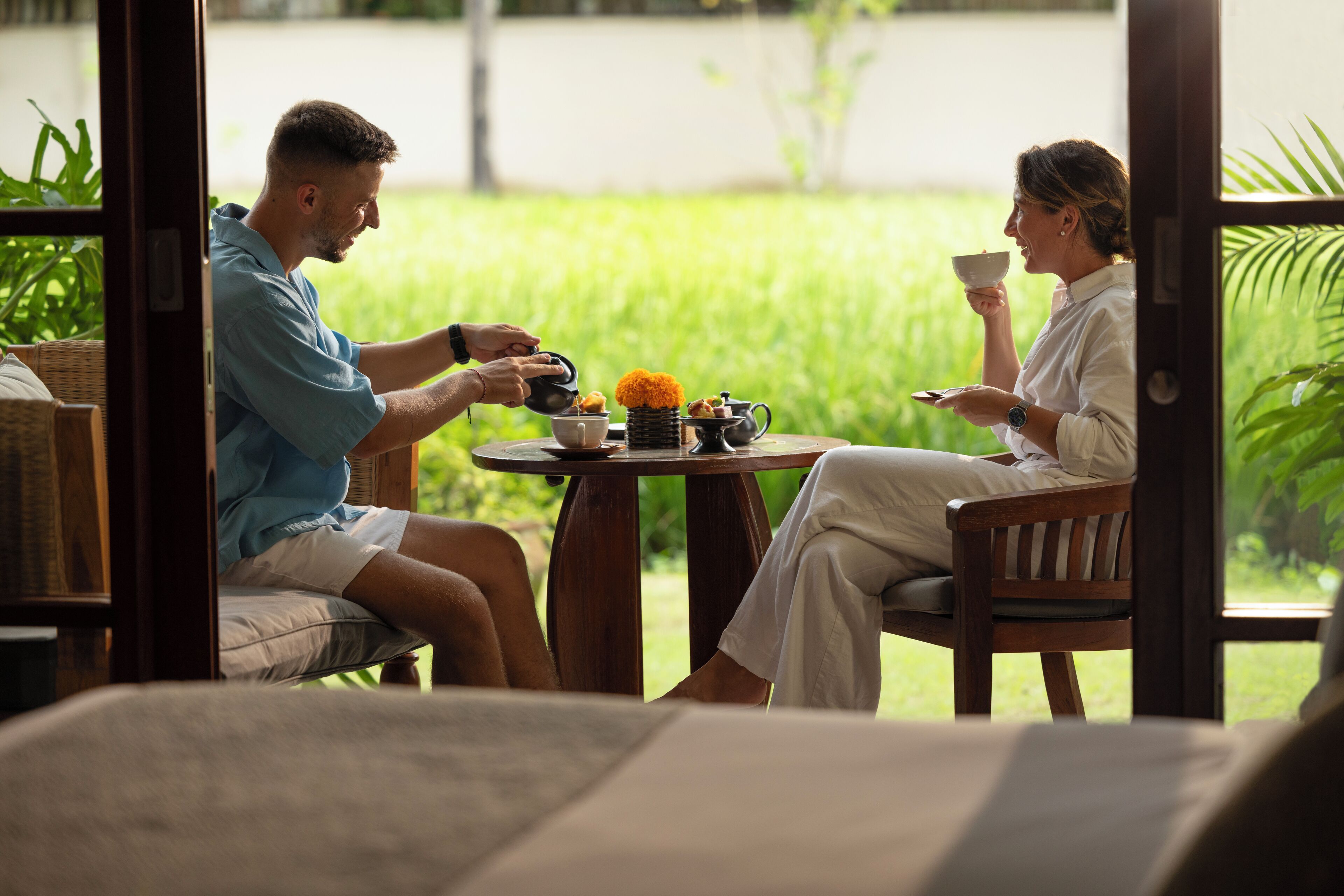 A couple seated at a round wooden table with a view of a lush green garden.